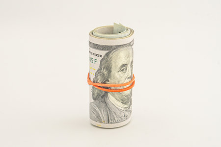 100 dollar bills on a roll isolated on white background. Rolled up money isolated on white background. Dollars isolated on white background. Dollar roll wrapped with red ribbon.の写真素材