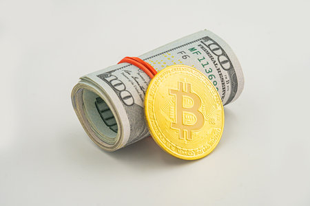bitcoin BTC coin and roll of dollar bills banknotes white background. American US dollar bills in rolls with silver Bitcoin coin.の写真素材