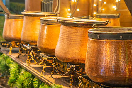 A row of increasing copper kettles with handles and spouts, arranged in an industrial setting with dim lighting, some greenery, warm tone, and a focus on texture and detailの写真素材