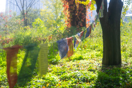 A tranquil outdoor scene with colorful banners swaying gently, forming a canopy The backdrop is a lush park or garden, with an urban environment visible in the blurred background The image style coの写真素材
