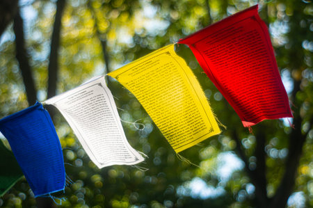A row of colorful, cascading wind catchers or prayer flags hangs outdoors with a blurred tree background The vibrant, multi-colored banners have legible messages printed on themの写真素材