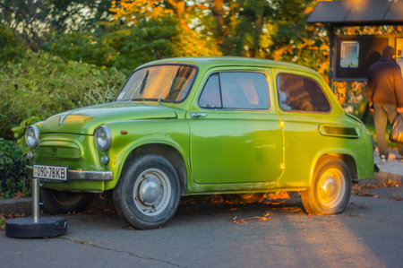 An older, vibrant green car with round headlights and side windows is parked on a public space Possibly taken in early morning or late afternoonの写真素材
