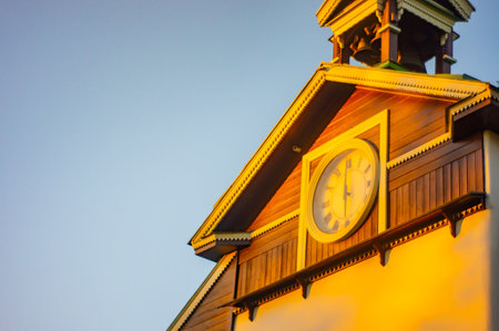 Image of an old-fashioned church or public building, bathed in golden sunlight Clock with roman numerals visible on the facade Wood siding, darker trim, and a bell tower are notable architectural dの写真素材