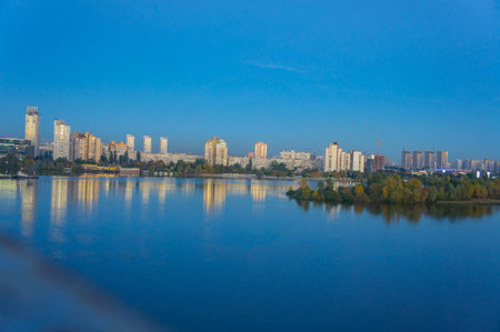 A tranquil night scene of a city skyline with tall buildings, reflecting in a body of water The transitioning sky conveys either sunrise or sunsetの写真素材
