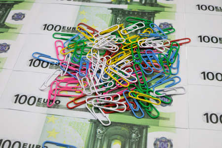 A pile of multicolored paper clips lies on a background of 100 Euro banknotesの写真素材