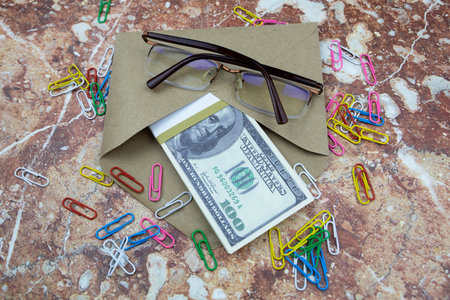 Glasses and an envelope with a bundle of 100 dollar bills lie on a stone tableの写真素材