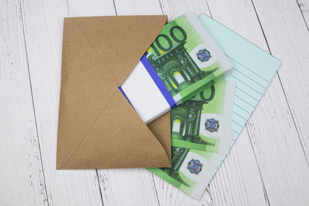 100 Euro banknotes in a brown envelope with a notebook lie wooden backgroundの写真素材