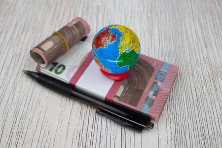 A small globe and a black pen lie on a pack of 10 Euro banknotesの写真素材