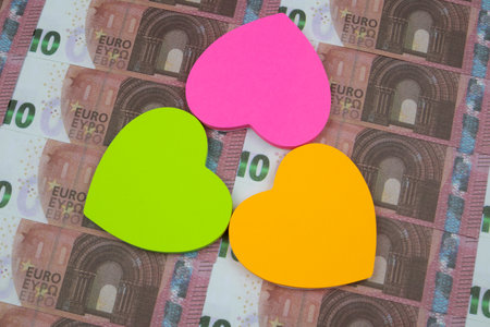 Three colored stickers in the form of hearts lie on 10 Euro banknotesの写真素材