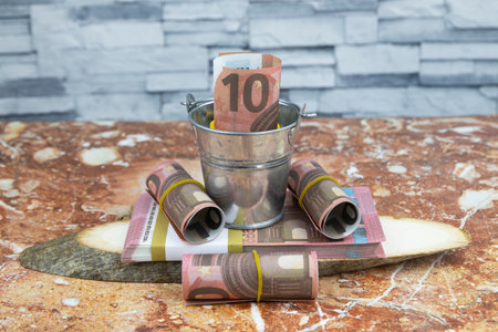 Rolls of 10 euro money and bundles of banknotes folded in a small metal bucketの写真素材