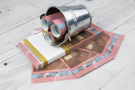 Financial still life with 10 Euro bills or banknotes in rolls in a metal bucket, a wad and fanned out over a grey floor viewed high angle. High quality photoの写真素材