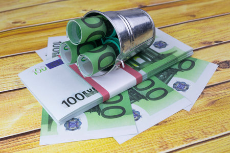 Financial still life with 100 Euro bills or banknotes in rolls in a metal bucket, a wad and fanned out over a grey floor viewed high angle. High quality photoの写真素材