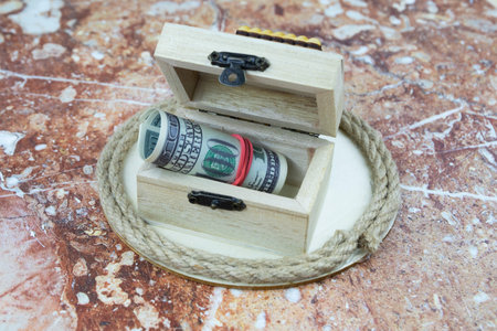 Conceptual financial still life with model house and rolled 100 USD banknotes on small wooden drawers with coiled rope for house ownership, costs or property themesの写真素材