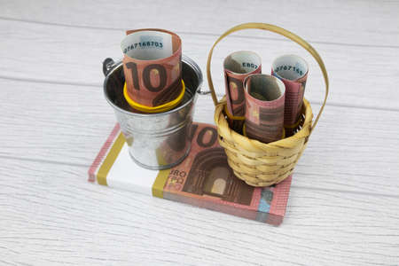 Rolled 10 euro banknotes stand in a small bucket and basket on a bundle of banknotes. High quality photoの写真素材