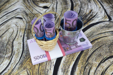 Rolled 500 euro banknotes stand in a small bucket and basket on a bundle of banknotes. High quality photoの写真素材