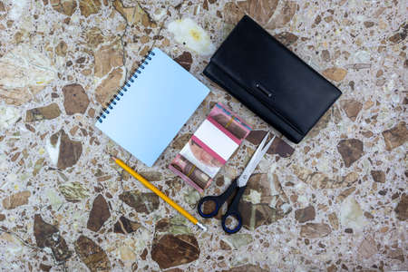 Business or office concept on decorative marble background with purse, scissors, notebook and wad of...