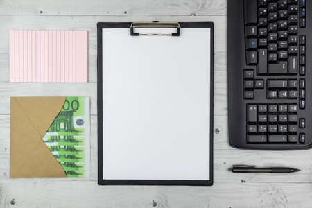 Business success or payment concept with workstation with blank notepaper on a clipboard, notebook, keyboard and and Euro bills in an envelope in a top down view. Flat layの写真素材