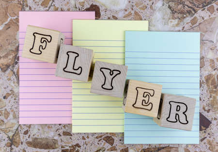 Flyer concept with alphabet letters on wooden blocks or cubes placed over three colored sheets of notepaper on a marbled stone background. Flat layの写真素材