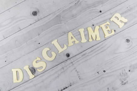 Disclaimer concept with undulating word in alphabet letters arranged diagonally on light grey planks background viewed as a flat lay still life with copyspaceの写真素材