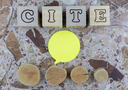 Cite concept with alphabet letters on wooden cubes and blank yellow speech bubble for a quote above a row of wood cross sectionsの写真素材