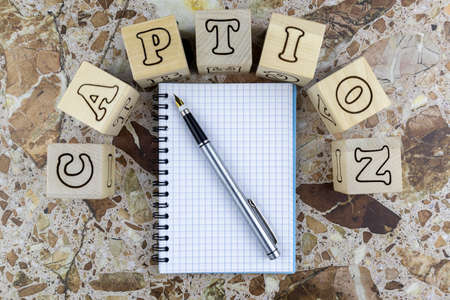 Caption concept with notebook and pen below arched alphabet letters on wooden cubes on a marbled...
