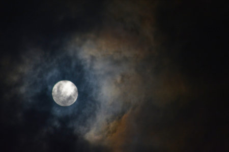 Artistic moonlit sky showing a full moon surrounded by textured clouds with subtle blue and warm...