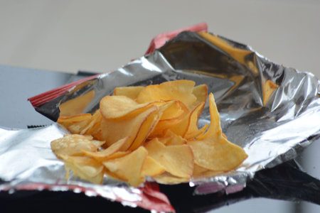 Male hand selecting a single potato chip over an open silver foil snack bag concept of snacking...
