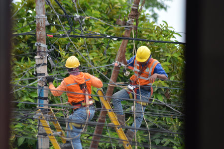 Electric utility workers performing maintenance on overhead power lines while using safety gear and ladders. Location and date Kediri Indonesia February 13 2026. The scene shows technicians working at height to repair electrical cables and infrastructure. Ideal for themes related to electricity, utilities, industrial safety, engineering, construction, maintenance services, and outdoor technical work.の写真素材