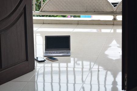 Laptop placed with two smartphones on a shiny tiled floor near a doorway and balcony showcasing a...