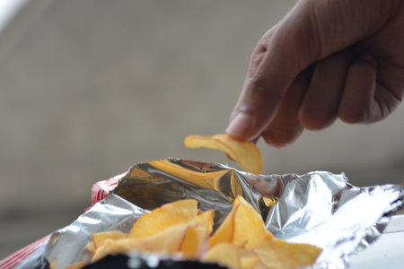 Close up of hand lifting a single potato chip from an open foil snack bag representing choice portion and snacking lifestyle suitable for editorial and adsの写真素材