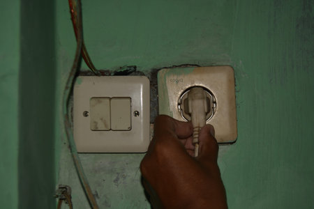 A hand removing a power cable from a worn electrical wall socket. Useful for illustrating energy...