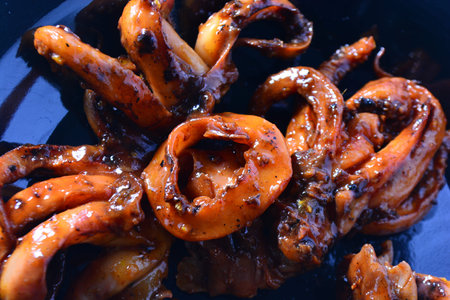 Macro of a calamari ring and curled tentacles with sticky sauce on a bright green surface evoking...