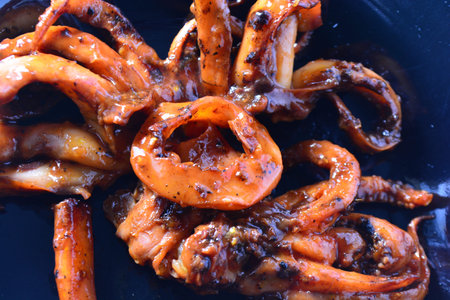 Overhead close up of grilled squid with glossy sauce on a dark background. Strong contrast ideal for...