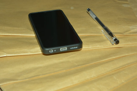 Generic smartphone and pen arranged on brown paper desk surface representing business planning and...