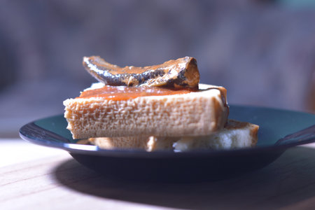 Close up view of sardine sandwich on white bread with spicy sauce on a black plate. Homemade meal...