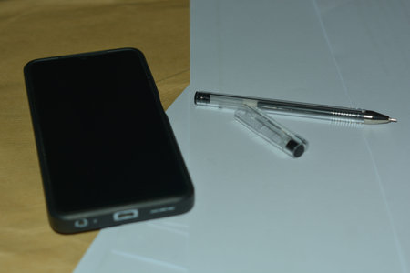 Close view of a generic smartphone and clear pen resting on white paper representing clean office...