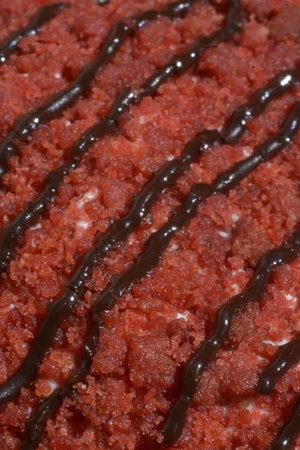 Macro view of red velvet dessert surface showing crumbs and diagonal chocolate drizzle decoration