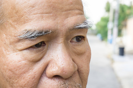 Closeup old asian man's eye and eyebrow. with copy space for text. aging concept., Old asian man glabrous head., stand on the street with copy spaceの写真素材