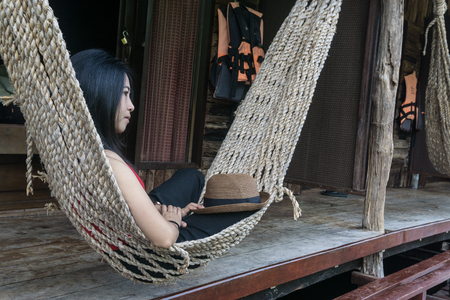 young caucasian asian girl swinging in a hammock in a pleasant laziness of a weekend evening. she is smiling through her beard., holiday at riverside in Thailand., close up asian girl relax face.の写真素材
