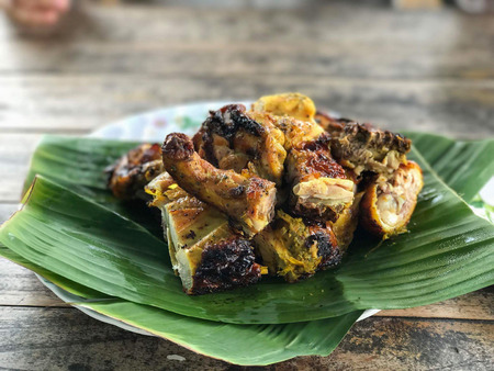 Grilled chicken on banana green leaf with plate and wooden table background., with spicy sauce. Thai traditional food.の写真素材