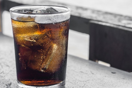Glass of cola with ice on wooden table., with blur river outdoor background., hot concept. thirsty concept.の写真素材