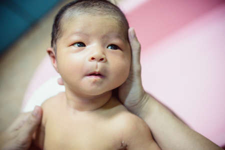 Newborn baby taking a bath by mother at home, asian child.の写真素材