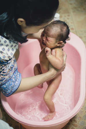 Newborn baby taking a bath by mother at home, asian child.の写真素材