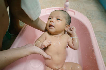 Newborn baby taking a bath by mother at home, asian child.の写真素材