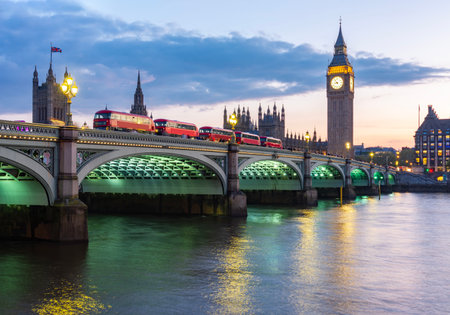 Big Ben tower of Houses of Parliament and double-decker buses on Westminster bridge at sunset,...
