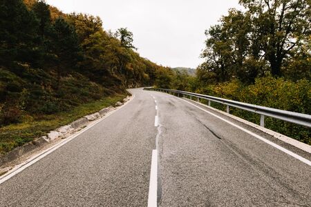 Winding mountain road in a lush forest landscape in autumn with cloudy skyの写真素材