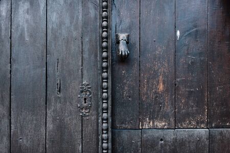 Detail of a typical medieval dark wooden door with a lock and a knob in the shape of a cast iron or bronze hand and carved wooden ornamentsの写真素材