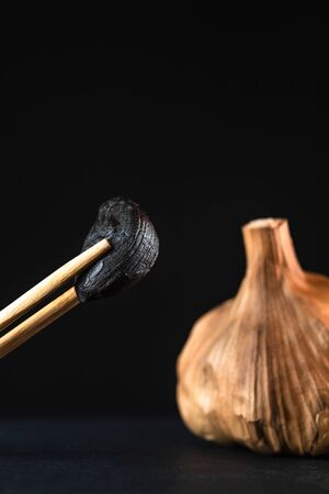 macro photography of black garlic clove with chopsticks, garlic head and black background.の写真素材