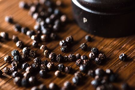 Macro photography of black peppercorns and grinder in diagonal composition on rustic wooden background.の写真素材