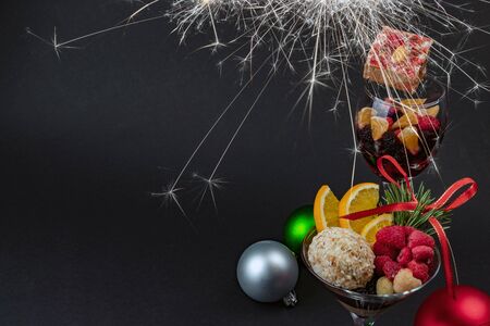 Holiday sweets and fruits in a glass and christmas toys on a black background with sparklerの写真素材